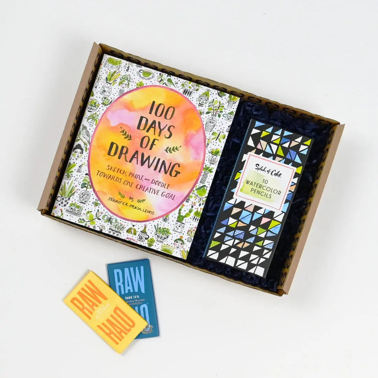 A get well soon gift package open to reveal a drawing book, watercolour penciles, and some raw halo chocolate bars