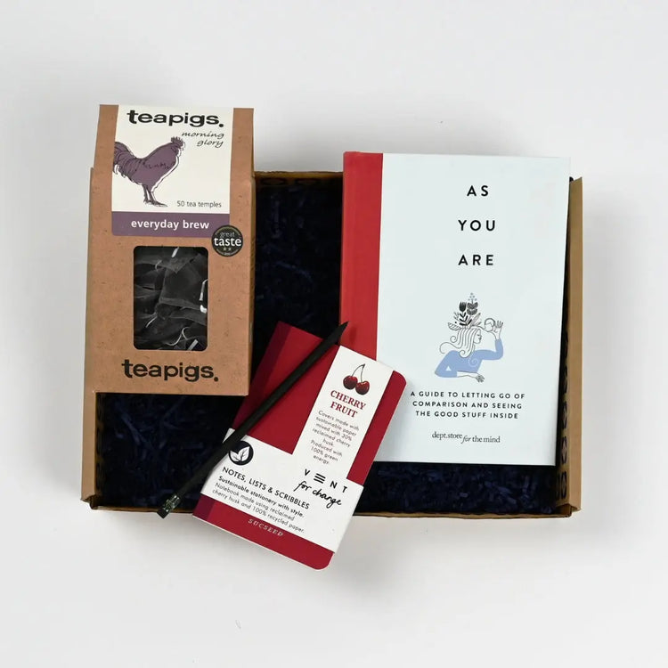 A gift package containing a book titled 'As You Are', a packet of tea, and a small red and white notebook, all presented in a kraft gift box.