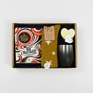 A gift box containing a variety of items including a packet of luxury hot chocolate, a pair of cozy wool socks, and a heart-shaped candle, all arranged for a thoughtful gift presentation.