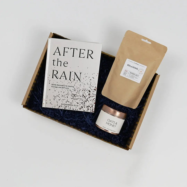 A gift package containing a book titled 'AFTER the RAIN', a scented candle, and a herbal tea blend, all packaged in a box with blue tissue paper.