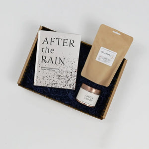A gift package containing a book titled 'AFTER the RAIN', a scented candle, and a herbal tea blend, all packaged in a box with blue tissue paper.