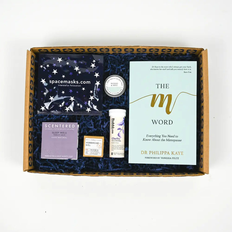 A gift package containing a face mask, a book titled 'The M Word', and other wellness items, presented in a cardboard box with blue confetti lining.