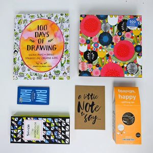 A collection of items including a drawing book, water-color pencils, a box of tea, and a jigsaw puzzle with colorful floral and animal patterns.