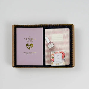 A gift box open to reveal a pink journal, a small bottle of perfume, and a packaged candle, all arranged neatly inside.