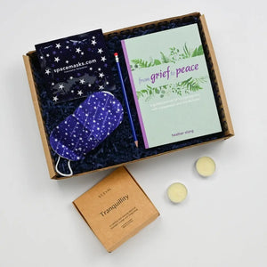 A gift box containing a book titled 'From Grief to Peace', a lavendar facemask, pencil, and a box of st eval tealights