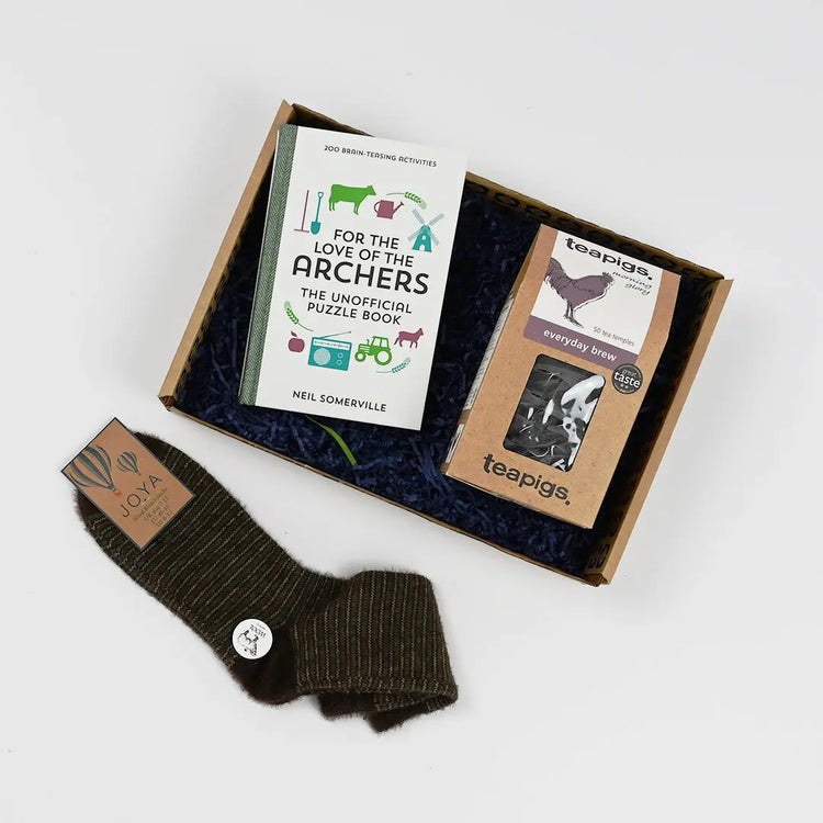 A gift box containing a puzzle book titled 'For the Love of the Archers', a Teapigs tea bag, and a pair of socks, all arranged on a bed of blue tissue paper.