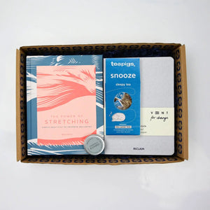 A gift box open to reveal its contents, which include a stretching guide, a snooze boxof tea bags, a notebook and a grapefruit lip balm