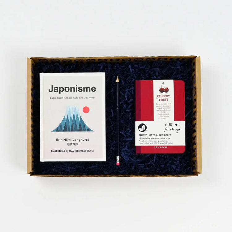 A gift package containing a book titled 'Japonisme', a notebook, and other items related to wellness and self-care, presented in a box with a blue sizzle filled gift box