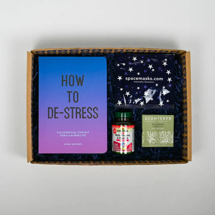 A gift package containing a book titled 'HOW TO DE-STRESS', a small bottle, and what appears to be a packaged food item, all presented in a box with a hand-written note.